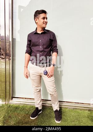 Full body of handsome Indian young man in smart casuals looking away and standing on sunny summer day Stock Photo