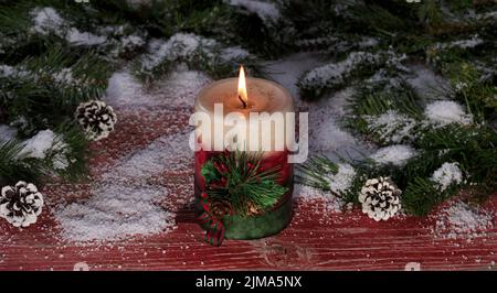 Burning candle on snowy rustic red wooden boards with Christmas decorations Stock Photo