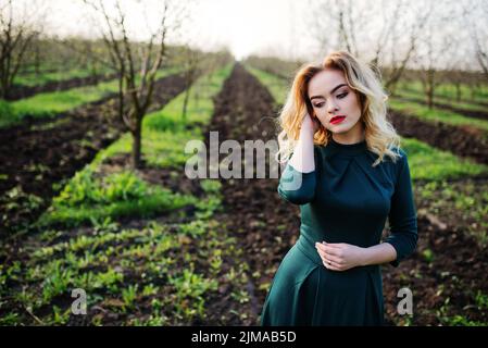 Yong elegance blonde girl at green dress on the garden in spring. Stock Photo