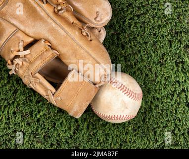 Close up overhead view of old leather baseball and mitt on grass turf field Stock Photo
