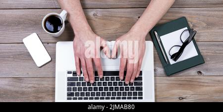 Top view of working desktop with hands on laptop keyboard with other office objects Stock Photo