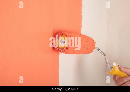 peach wall painting, hand with roller the concept of renovation in the room. Stock Photo