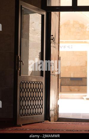 Ancient wooden gate, engraved door, gate opening inside the mosque in Mardin, hot summer day, silhouette of people reflection on the door. Stock Photo