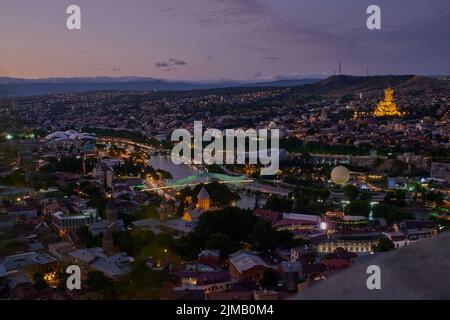 Tbilisi, Georgia night Panoramic view from top of fortress of Narikala showing the bridge of peace, Rike Park, Kura River and Holy Trinity Cathedral Stock Photo