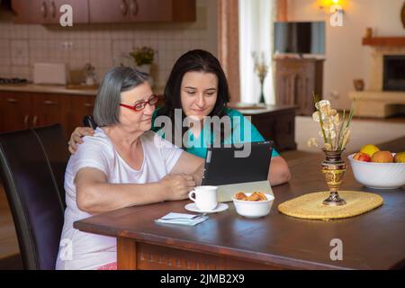 Caregiver with elderly woman using digital tablet at home Stock Photo