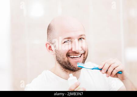 Smiling bald man holding toothbrush with toothpaste and brushing teeth Stock Photo