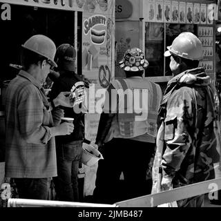 A grayscale shot of construction workers stopping for a lunch at a hot dog stand in NYC, United States Stock Photo