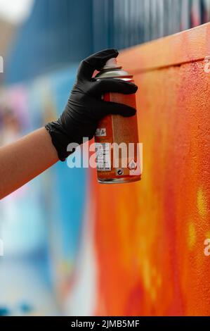 a Close-up vertical shot of a hand wearing black glove using spray paint on a brightly colored mural Stock Photo
