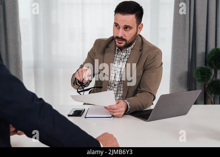 Confident businessman discussing over contract with partner. Male professionals planning in meeting. They are sitting at office desk. Stock Photo