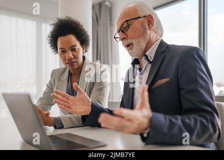 Confident male and female professionals brainstorming over laptop. Business executives discussing during meeting. They are sitting at desk while worki Stock Photo
