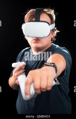 A young man playing games wearing virtual reality goggles on a black background Stock Photo