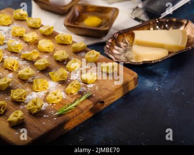 Cooking homemade Italian ravioli from flour (dough) and minced meat filling on a blue background. Ravioli on a wooden cutting board. Dumplings, stuffe Stock Photo