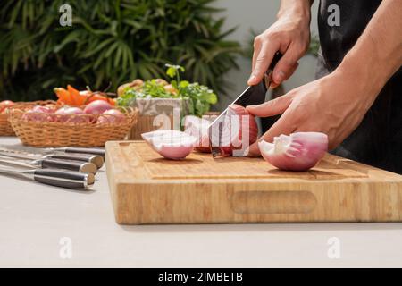 Close up view of the hands of a man chopping onions in a table in a garden Stock Photo