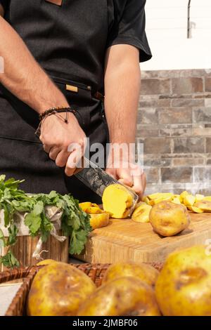 Vertical photo of an unrecognizable man chopping potatoes in a table with parsley in a garden Stock Photo