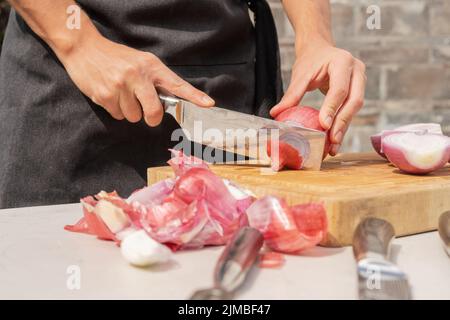 Cropped photo of the hands of a man chopping onions on a wooden board outdoors Stock Photo