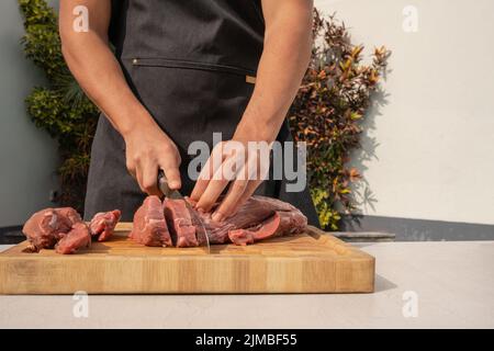 Close up photo of the hands of a man cutting meat using a knife in a table of a garden Stock Photo