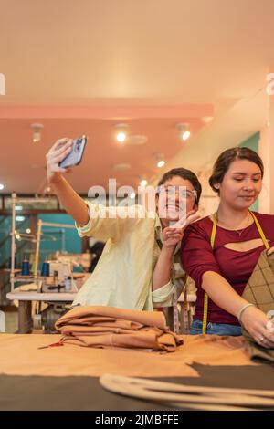 Vertical portrait of two female colleagues taking a selfie in a sewing workshop Stock Photo