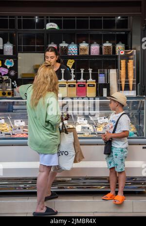 mother and child standing at an ice cream parlor or kiosk at the seaside buying ice creams to cool down during a hot summer heatwave Stock Photo