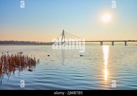 Foggy sunrise on Dnieper River with a view on sun path on the rippled water surface of water and Pivnichnyi (Northern) Bridge in background, Kyiv, Ukr Stock Photo