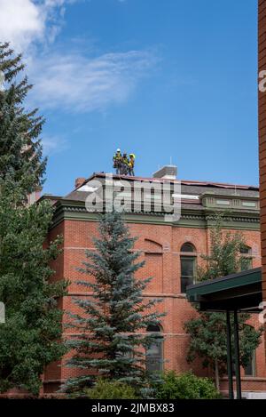 Construction workers stand on the mansard roof of the red brick Pitkin County Courthouse in Aspen, Colorado, Stock Photo