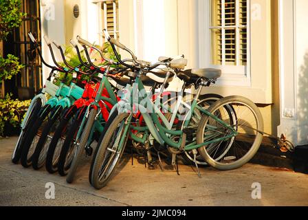 A row of rental bikes are chained to a bike rack at a store that rents them to tourists in Charleston South Carolina Stock Photo