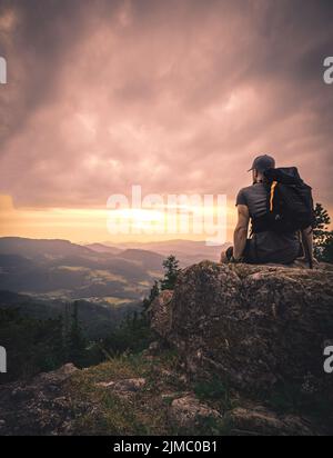 Man silhouette stay on sharp rock peak. Satisfy hiker enjoy view. Tall man on rocky cliff watching down to landscape Stock Photo