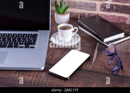 Laptop notebook with blank screen and cup of coffee and notepad pen and books and smart-phone on wooden Stock Photo