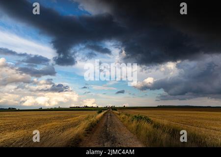 Dramatic storm clouds over fields. Country landscape. Windy weather. Plain field against the background of dark sky. Stock Photo