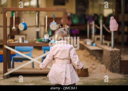 Toddler girl with pigtails at day care center wearing cute pink coat, no face Stock Photo