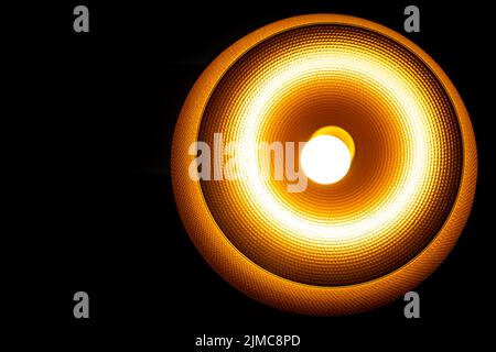A Modern lamp hanging down from ceiling in the dark background. Minimalist chandelier with glowing warm light from bulb. Stock Photo