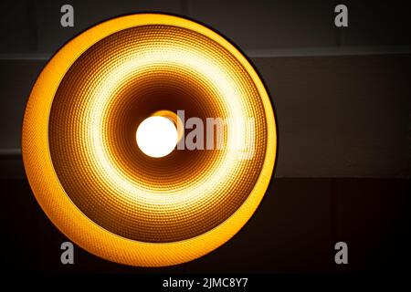 Modern lamp hanging down from ceiling in the dark background. Minimalist chandelier with glowing warm light from bulb. Stock Photo