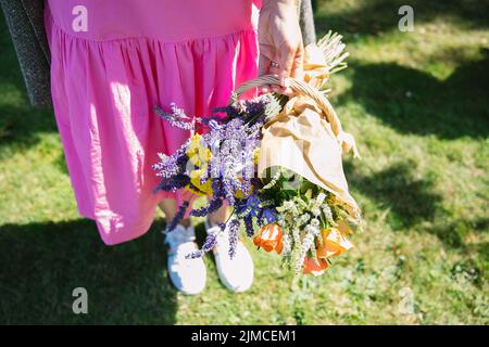 summer bouquet of yellow yarrow and lavender bouquet in woman's hands shot from above, woman wearing a pink dress Stock Photo