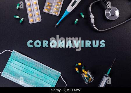 Protective masks, medicines, thermometer, stethoscope and syringe with coronavirus text on a black background Stock Photo