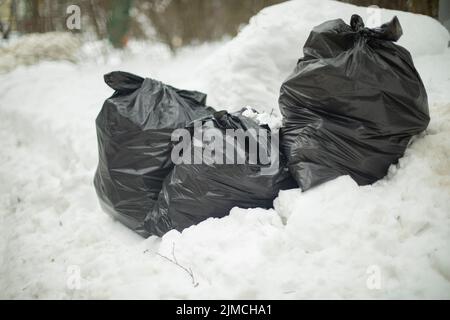 Black bags in snow. Garbage on road. Waste in bags. Throwing out garbage on street. Illegal landfill. Stock Photo