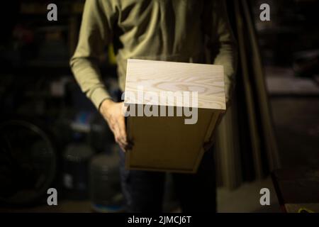 Box of wood in hand. Production of furniture from boards. Wooden wardrobe. Details of work. Result of board processing. Stock Photo