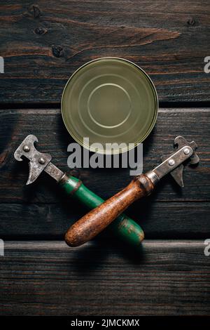 Top view of tin can on a wooden background with can opener Stock Photo