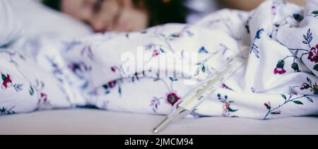 Woman  in bed with fever focus on thermometer coronavirus or COVID-19 sympthoms Stock Photo