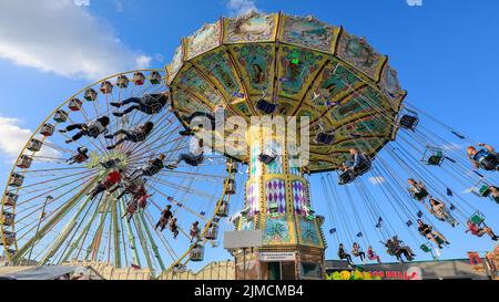 Crange, Herne, NRW, 05th Aug, 2022. People enjoy their ride on a beautifully decorated traditional merry-go-round against the fair backdrop with the Jupiter ferris wheel. The official opening day of the 2022 Cranger Kirmes, Germany's 3rd largest funfair and the largest of its kind in NRW, sees thousands of visitors enjoying the carousels, roller coasters, beer halls, food stalls and other attractions. Credit: Imageplotter/Alamy Live News Stock Photo