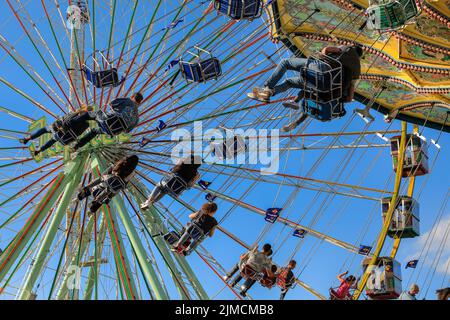 Crange, Herne, NRW, 05th Aug, 2022. People enjoy their ride on a beautifully decorated traditional merry-go-round against the fair backdrop with the Jupiter ferris wheel. The official opening day of the 2022 Cranger Kirmes, Germany's 3rd largest funfair and the largest of its kind in NRW, sees thousands of visitors enjoying the carousels, roller coasters, beer halls, food stalls and other attractions. Credit: Imageplotter/Alamy Live News Stock Photo