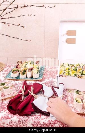 Crop anonymous person arranging napkins on table with set of fresh delicious tortilla rolls served for festive event celebration Stock Photo