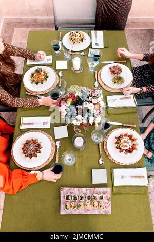 From above of crop anonymous friends having dinner while sitting at table with tasty salads and wineglasses served on terrace Stock Photo