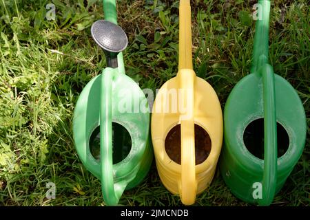 Row of three colorful watering cans in a garden Stock Photo