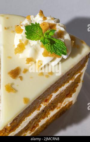 From above close up of slice of tasty sweet carrot sponge cake with cream decorated with mint leaf served on plate with spoon on table on white backgr Stock Photo