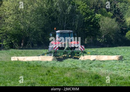 Red tractor mowing tall green grass in early spring in the Netherlands Stock Photo