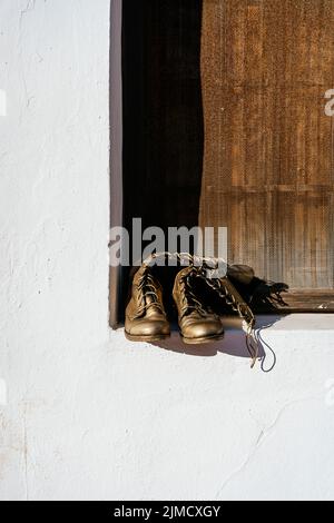 Bronze colored boots with shoelaces placed on windowsill with wooden shutters on sunny day on street Stock Photo