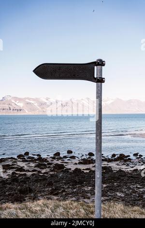 Signpost with pointer located on shore of Westfjords peninsula near rippling sea against mountain ridge in coastal area of Iceland Stock Photo
