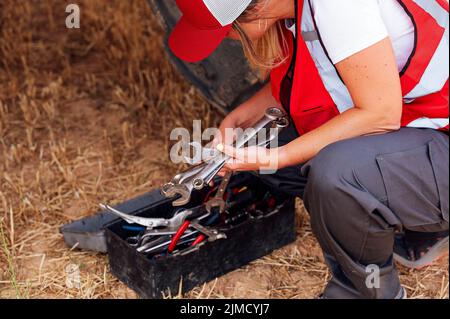 From above of crop unrecognizable female worker in uniform choosing tools from box while hunkering down on agricultural field in countryside Stock Photo