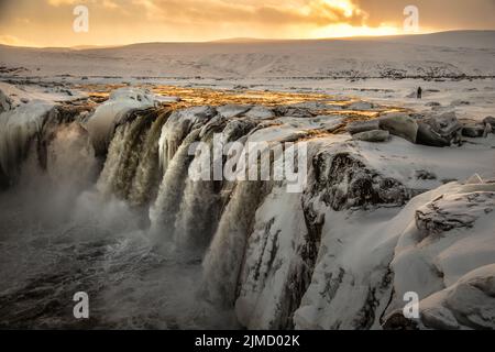 Majestic view of rapid waterfall flowing down frozen rocky mountain in winter in Iceland during sunset Stock Photo
