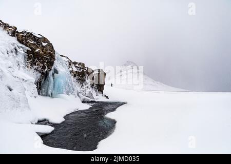 Distant travelers walking on hilly shore of frozen lake located in snowy highland terrain in Iceland