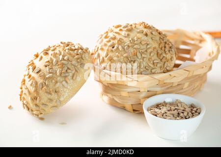 Freshly baked buns with sunflower seeds served in wicker bowl on white background Stock Photo